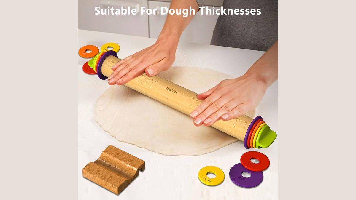 An adjustable rolling pin with thickness rings sits on a marble countertop for baking.