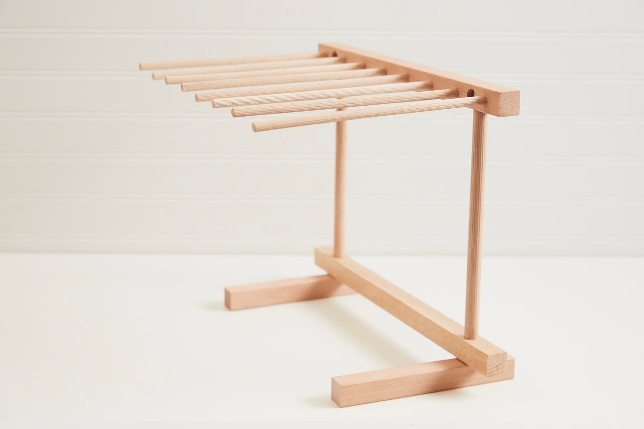 Collapsible pasta drying rack with fresh fettuccine on a wooden countertop in natural light.