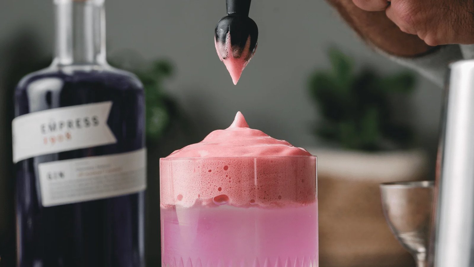A cream whipper beside a foam-topped cocktail on a marble bar counter.