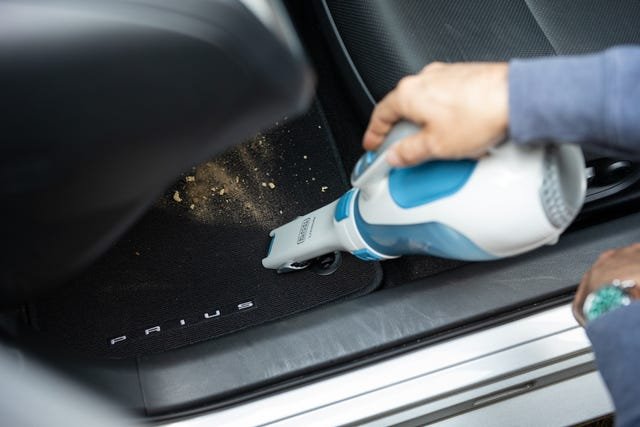 Handheld car vacuum cleaner resting on a car seat with microfiber cloth