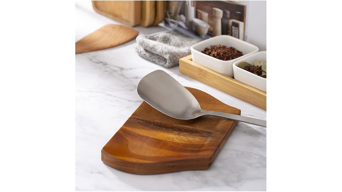 A modern double spoon rest holder sits on a marble countertop by a stove.