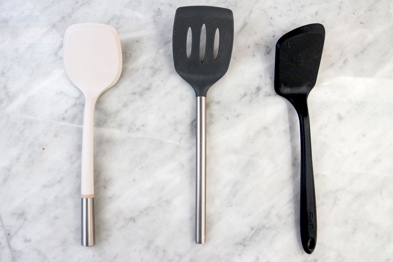 Nonstick nylon spatula set arranged on a wooden board beside a frying pan.