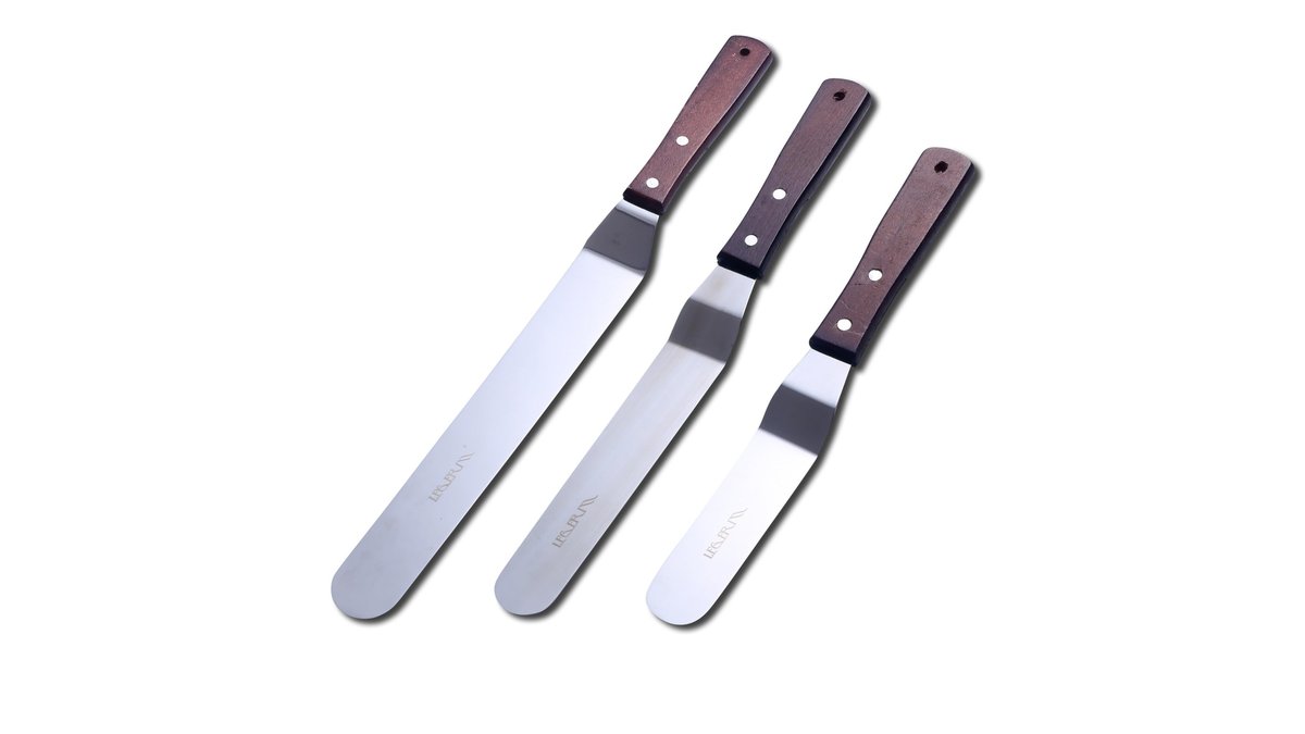 Offset spatula set for cake decorating resting on marble next to a frosted cake.