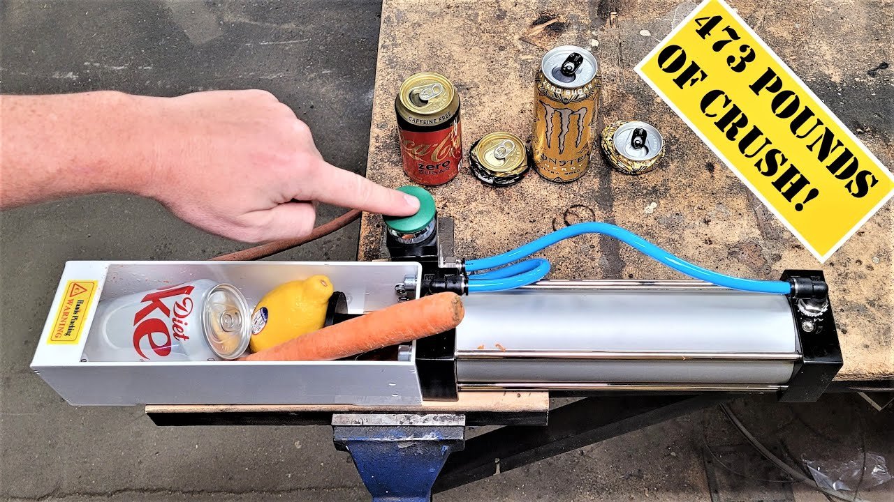 Pneumatic can crusher mounted on a garage wall above a bin of flattened cans.
