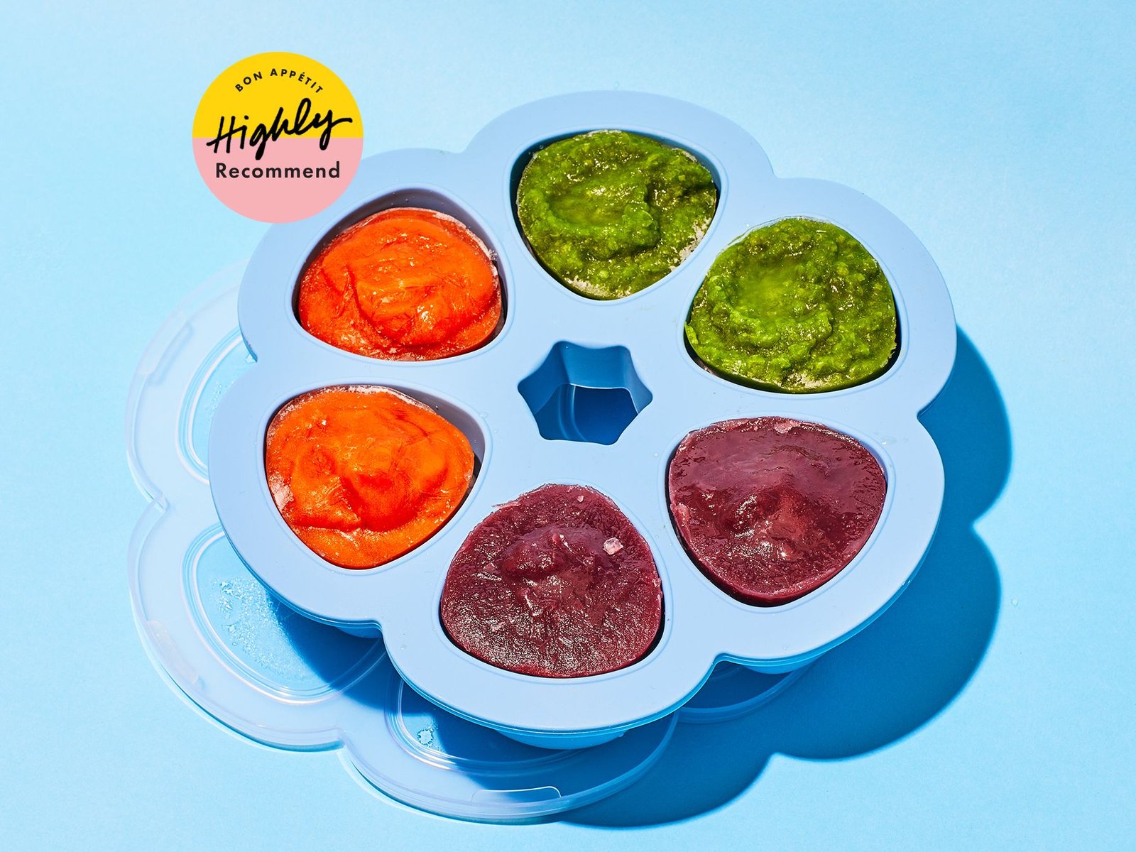 Rectangular silicone freezer tray filled with colorful pureed baby food cubes on a wooden counter.