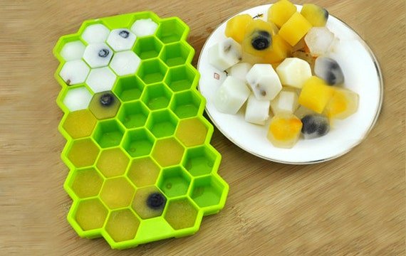 A silicone honeycomb ice cube tray with hexagonal ice cubes on a marble countertop.