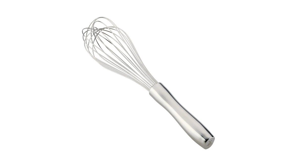 Stainless steel balloon whisk rests beside a bowl of whipped cream on a wooden board.