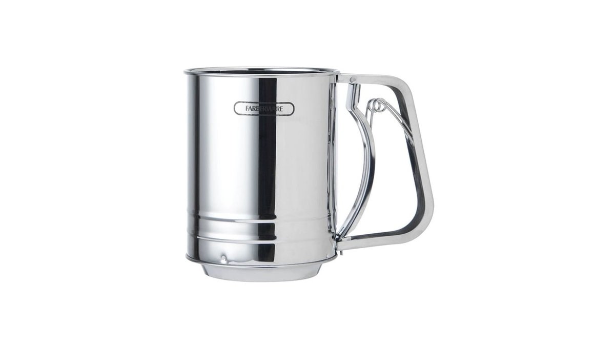 A stainless steel flour sifter sits on a wooden counter for baking preparations.