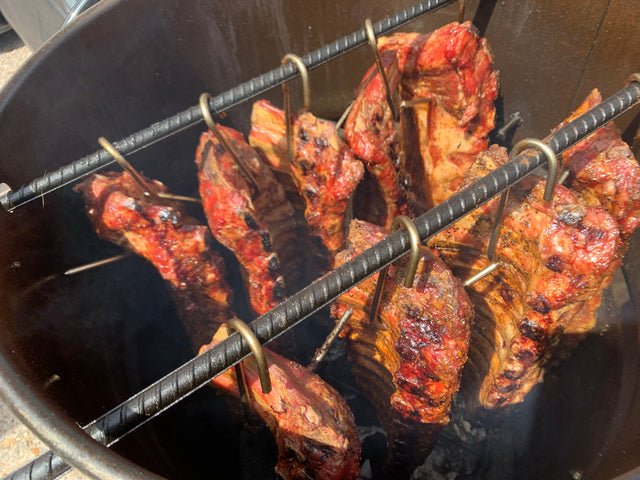 Stainless steel meat hooks on a wooden board next to a smoker grill