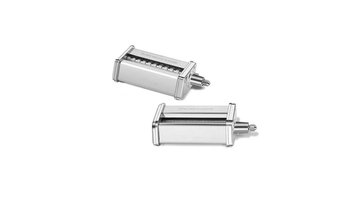 A stainless steel pasta maker attachment set sits on a floured wooden kitchen counter.